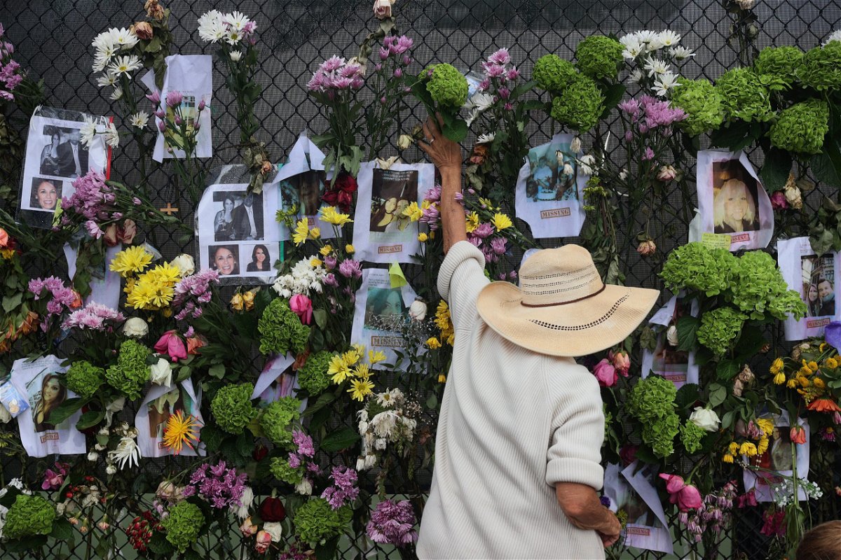 <i>Joe Raedle/Getty Images</i><br/>A person adds flowers to a memorial that has pictures of some of the missing from the partially collapsed Champlain Towers South condo building in Surfside.