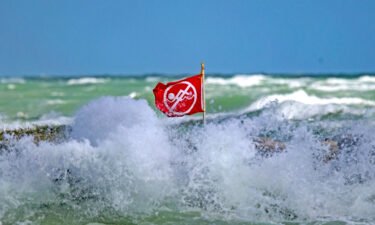 Waves crash around a no-swimming flag at Haulover Park beach in Miami Beach