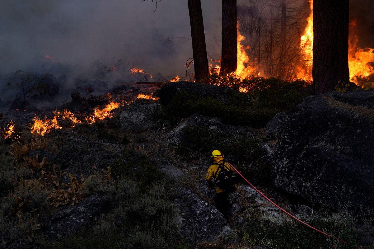 <i>Jae C. Hong/AP</i><br/>A firefighter carries a water hose toward a spot fire from the Caldor Fire burning along Highway 89 near South Lake Tahoe