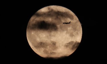A plane flies past the harvest moon as it rises behind the Statue of Liberty in New York City