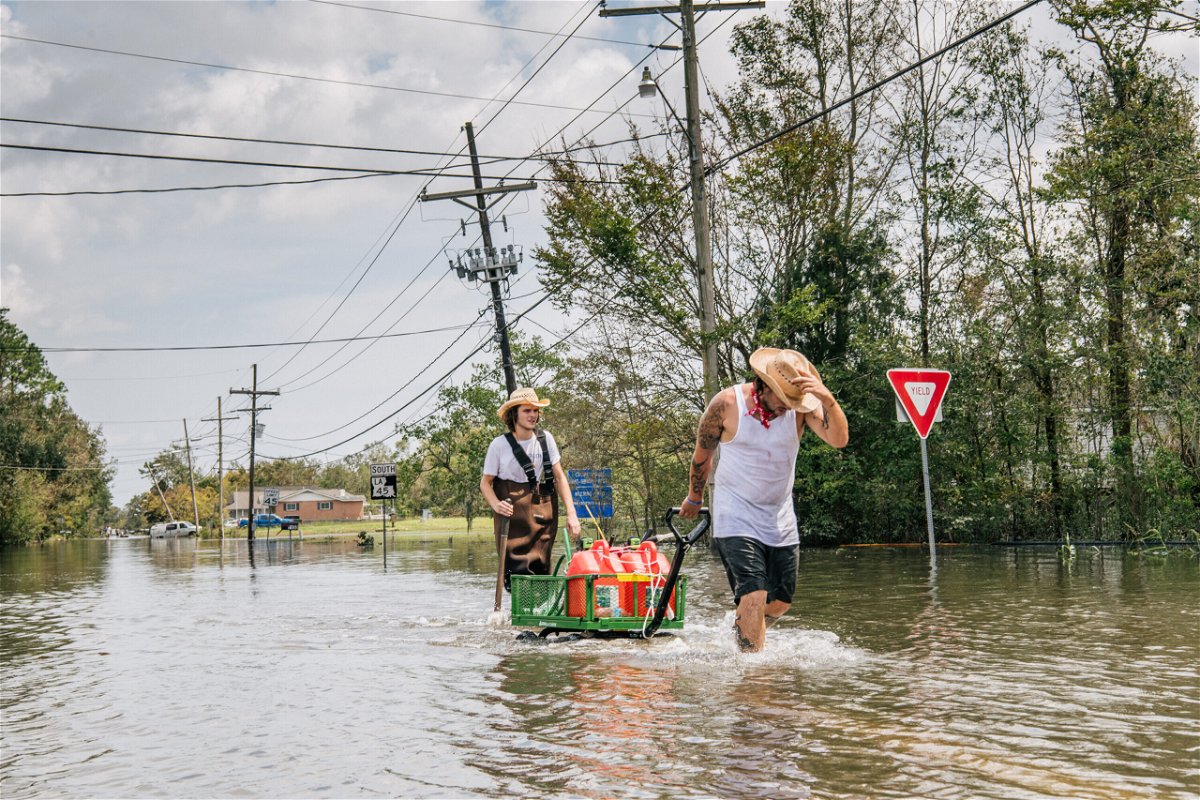 <i>Brandon Bell/Getty Images</i><br/>Residents move a cart with gas cans through a flooded neighborhood on Tuesday in Barataria