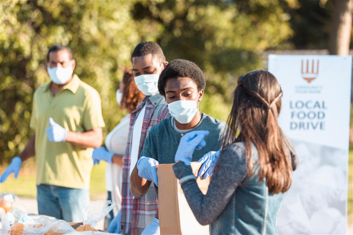 <i>SDI Productions/E+/Getty Images</i><br/>A young couple works together at the local food drive during COVID-19.  Everyone wears protective masks and gloves to slow the spread of disease.