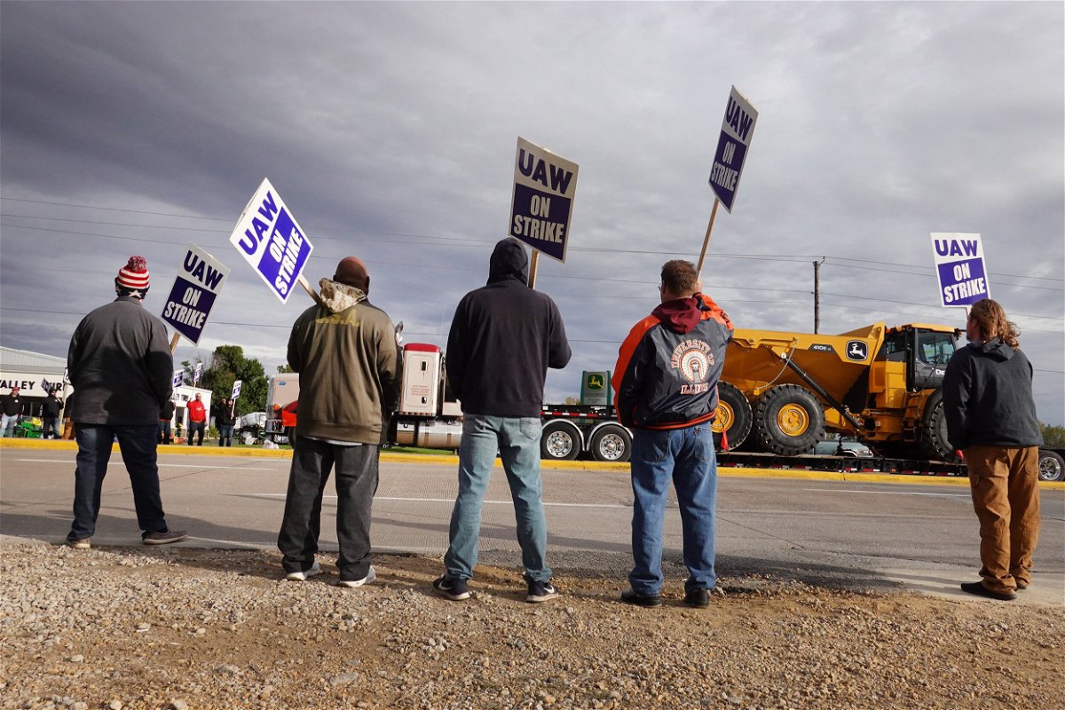 <i>Scott Olson/Getty Images North America/Getty Images</i><br/>A truck hauls a piece of John Deere equipment from the factory past workers picketing outside of the John Deere Davenport Works facility on October 15 in Davenport