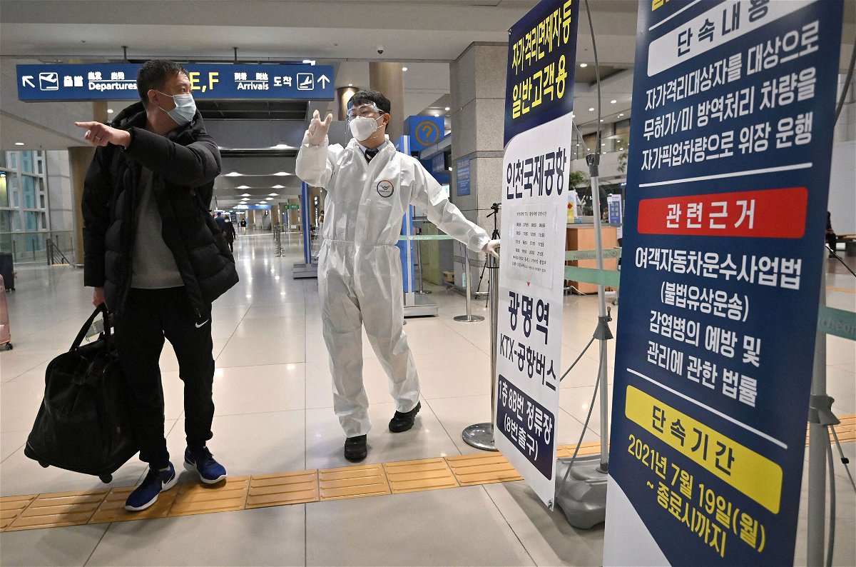 <i>Jung Yeon-je /AFP/Getty Images</i><br/>Global stocks and oil prices are falling again after a brief respite from the heavy sell-off triggered by the emergence of the Omicron coronavirus variant as a staff member wearing protective equipment guides a traveler at the arrival hall of Incheon International Airport on November 30 in South Korea.