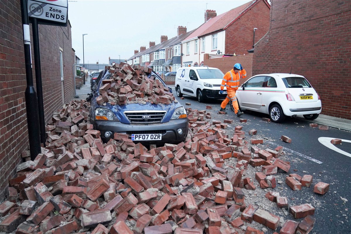 <i>Owen Humphreys/PA/AP</i><br/>A man walks past a car lying under fallen masonry from a property Sunderland