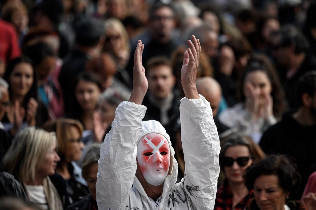 <i>Fabrice Coffrini/AFP/Getty Images</i><br/>A protester wearing a mask depicting syringes and a full protection suit applauses in Geneva on October 9.