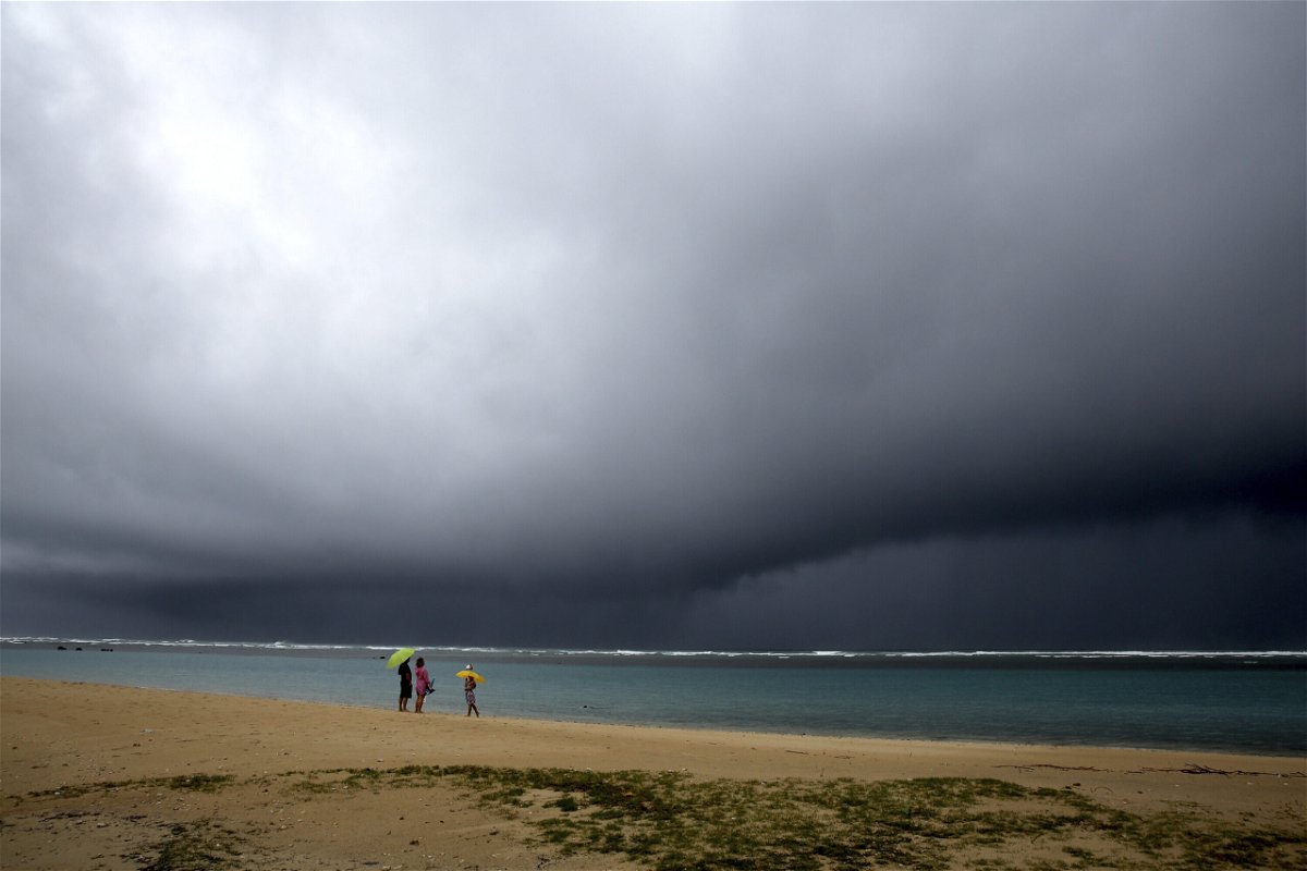<i>Caleb Jones/AP</i><br/>People hold umbrellas as it begins to rain on an otherwise empty beach in Honolulu on Dec. 6.