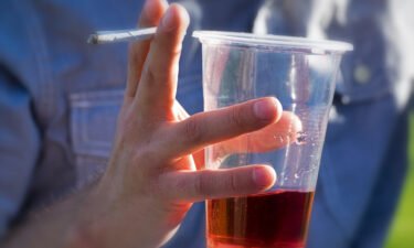A person drinks an alcoholic beverage while smoking cannabis. Adults who reported using cannabis and alcohol also said they drove under the influence of these drugs