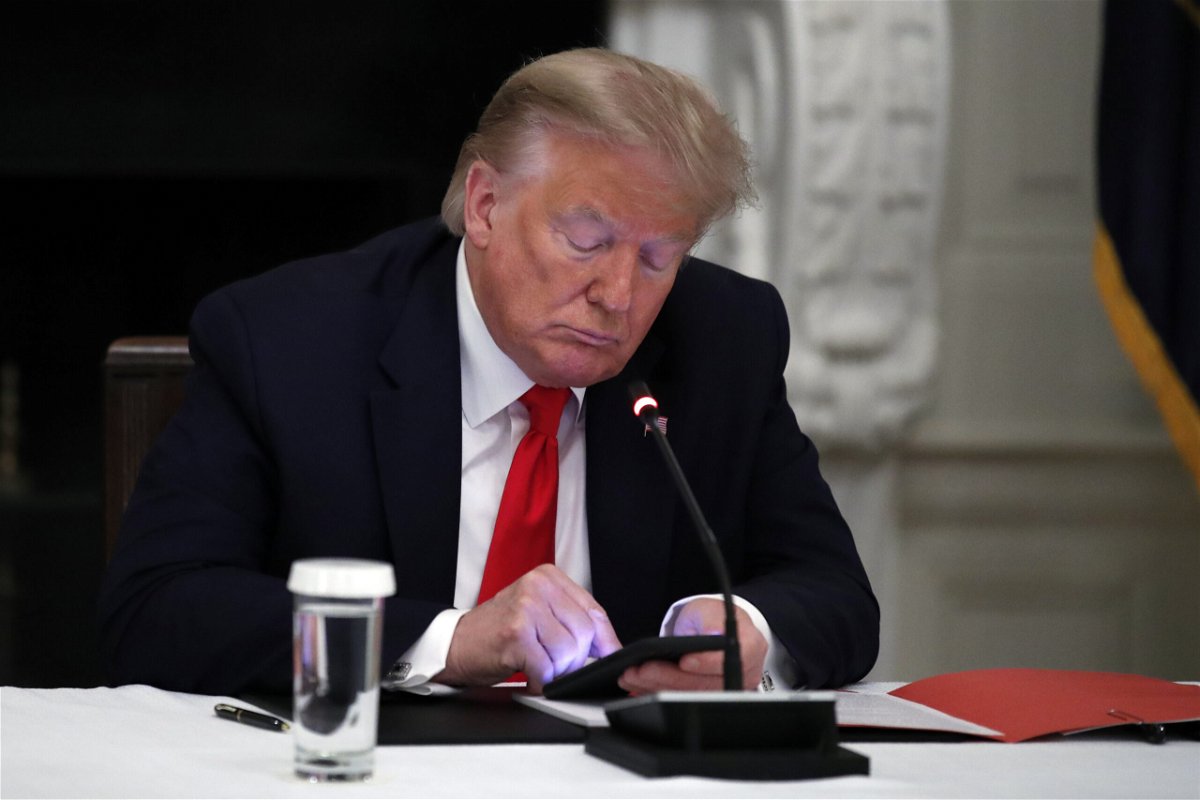 Former President Donald Trump looks at his phone during a roundtable with governors on the reopening of America's small businesses
