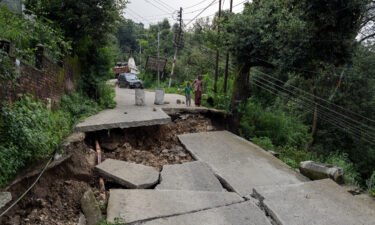 A woman and child look at a caved-in segment of a road damaged by heavy rain in Dharmsala