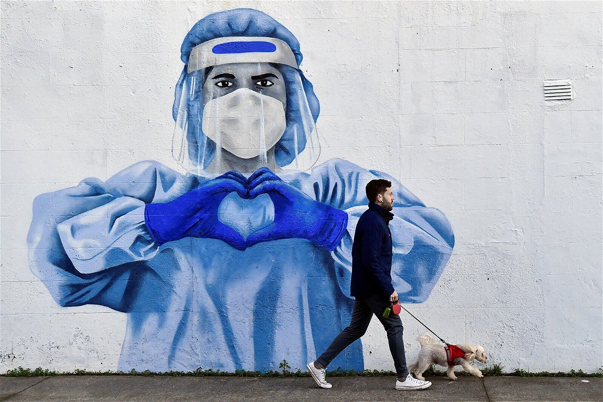 <i>Clodagh Kilcoyne/Reuters</i><br/>A man walks his dog past a mural depicting a frontline worker amid the spread of the coronavirus disease (Covid-19) in Dublin