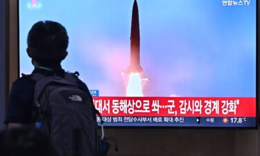 A man walks past a television screen showing a news broadcast with file footage of a North Korean missile test