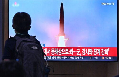 A man walks past a television screen showing a news broadcast with file footage of a North Korean missile test