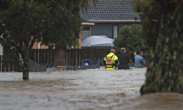 Emergency workers and a man wade through flood waters in Auckland