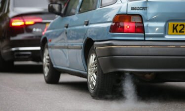 A car emits fumes from its exhaust as it waits in traffic in central London