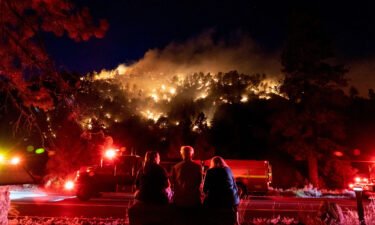 Residents watch part of the Sheep Fire wildfire burn through a forest on a hillside near their homes in Wrightwood