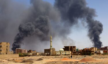 A man walks while smoke rises above buildings after aerial bombardment