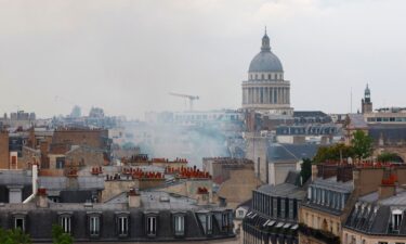 Smoke rises above rooftops with the Pantheon in the background.