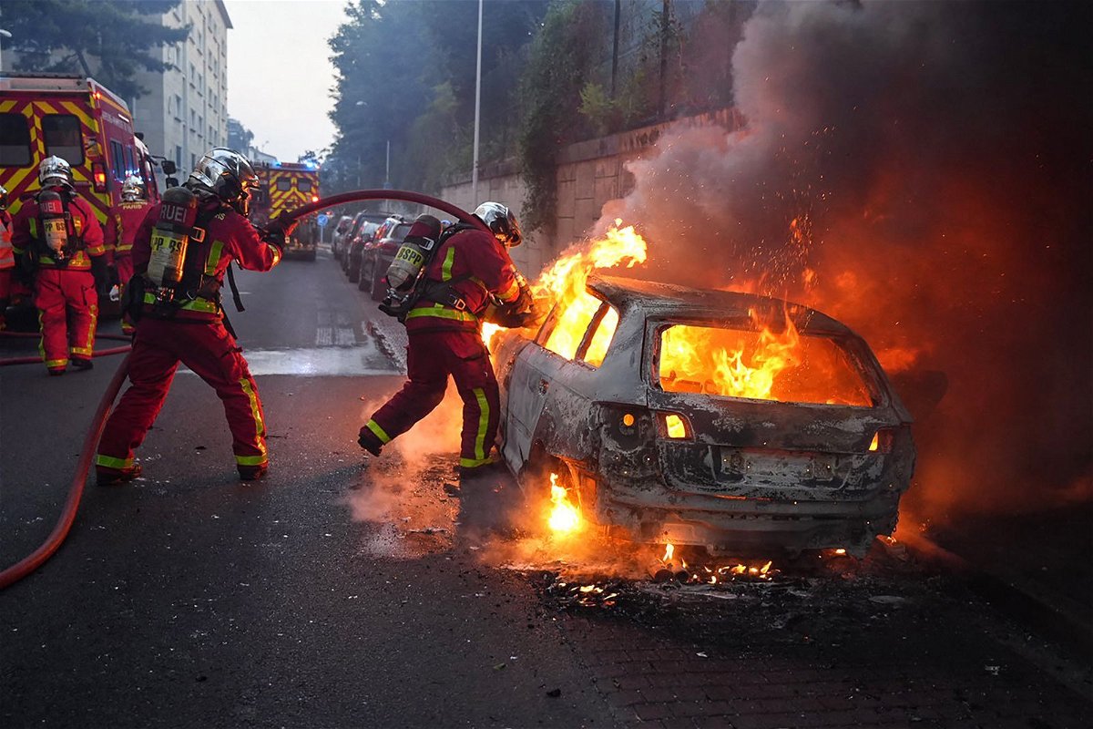 Firefighters work to put out a burning car at a protest in Nanterre