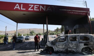 People stand near a burnt car