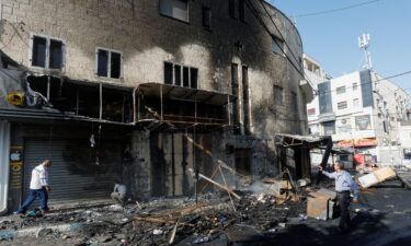 People walk past debris and a building damaged amid an Israeli military operation