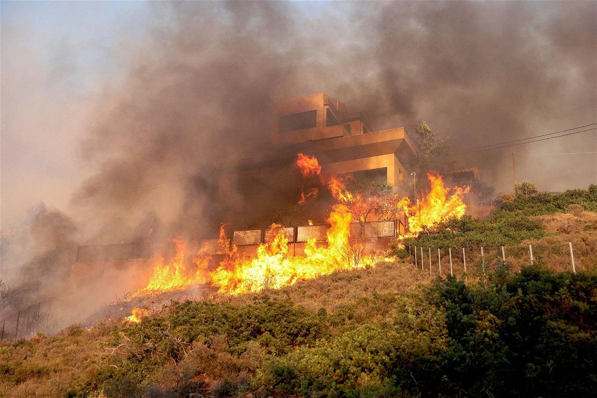 Flames engulf a house as a wildfire burns in Saronida