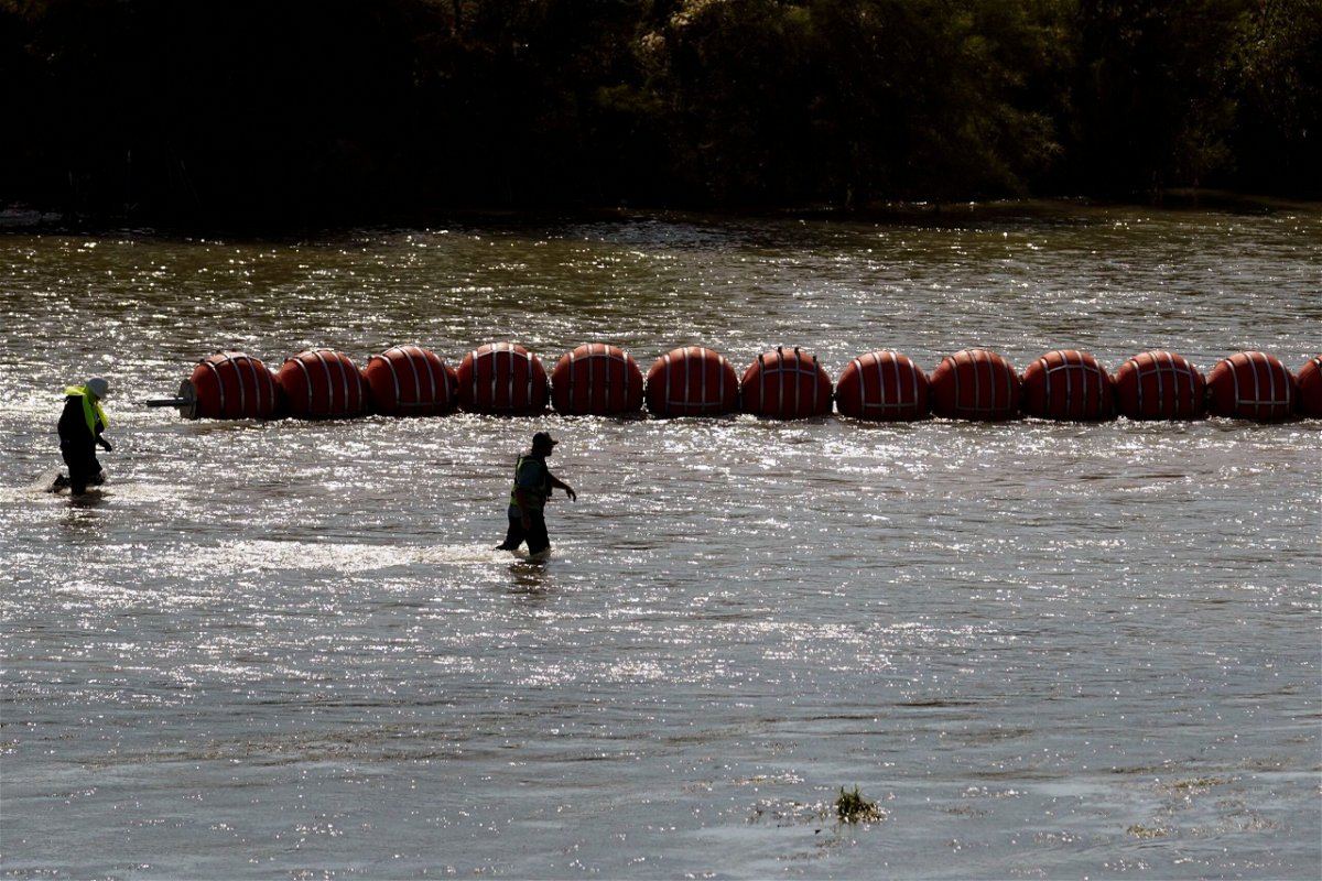 Workers help deploy a string of large buoys to be used as a border barrier at the center of the Rio Grande near Eagle Pass