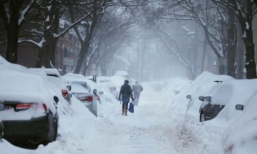 Pedestrians make their way along a snow-covered street during a storm in Cambridge